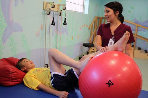 Staff performing leg therapy on boy with a large red ball